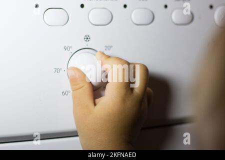 La mano di un bambino preme un pulsante su una lavatrice Foto Stock