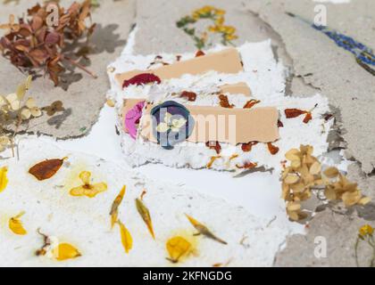 Il processo di generazione delle schede del posto di nozze dalla carta riciclata fatta in casa, dai fiori pressati e dalla cera di sigillatura. Tag personalizzati per il nome del matrimonio. Foto Stock