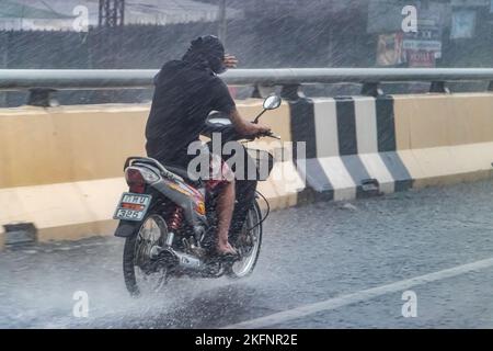 Ratchaburi, Thailandia, 14 2022 NOVEMBRE, Un giovane è in moto, scherzando gli occhi dalla pioggia pesante con la mano Foto Stock