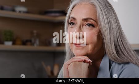 Primo piano testa ripresa ritratto sorridente donna anziana rilassante a casa mettere mento su palme ripiegate guardando in distanza sognando ricordi di momenti positivi Foto Stock