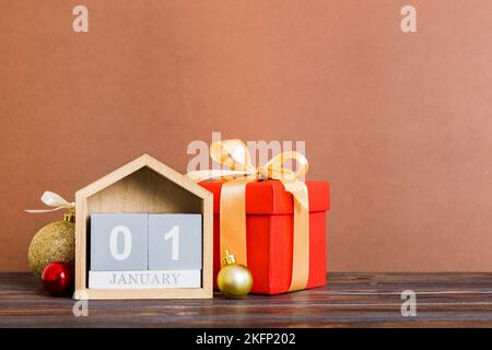 1 gennaio. Composizione natalizia su sfondo colorato con un calendario in legno, con una scatola regalo, giocattoli, spazio copia capiente. Foto Stock