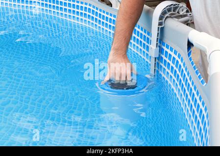 L'uomo pulisce lo skimmer per la piscina di telaio. Pulizia piscina contaminata. Foto Stock