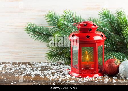 Lanterna rossa con una candela accesa e decorazione di Capodanno sulla neve e su sfondo di legno bianco con albero di Natale e spazio copia Foto Stock