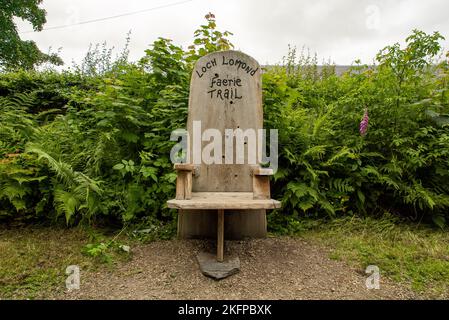 Una panchina in legno all'inizio del percorso Faerie a Loch Lomond, Scozia. Sedia da sentiero Loch Lomond Faerie / panca Foto Stock
