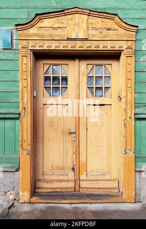 Vecchia porta in legno dipinta con sculture e due vetri in una parete verde della casa Foto Stock