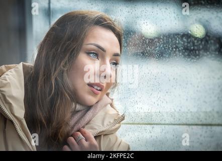 Una donna o un modello piuttosto giovane che attende sgombrosamente a una fermata dell'autobus in una giornata piovosa, Edimburgo, Scozia, Regno Unito Foto Stock