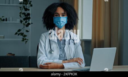 Primo piano ritratto donna africana in maschera di protezione medica femmina medico infermiera terapista chirurgo psicologo professionista seduto in ospedale clinico Foto Stock
