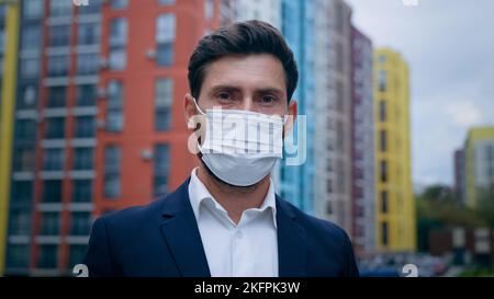Primo piano ritratto di un uomo d'affari che indossa una maschera medica messo sul respiratore faccia seguire le misure di quarantena uomo che lavora sulla strada della città uso personale Foto Stock