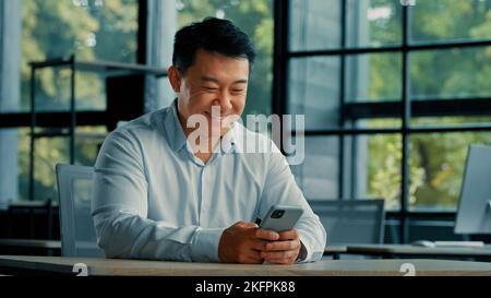 Uomo ritratto asiatico uomo imprenditore uomo datore di lavoro lavoro in ufficio guardare moderno gadget telefono cellulare schermo di ricerca informazioni on-line uso Foto Stock