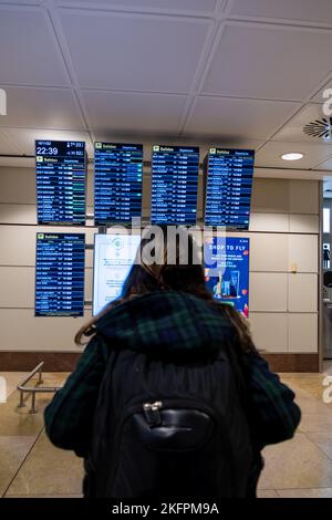 La giovane donna in piedi con il suo zaino guarda il programma alla stazione dell'aeroporto. Trasporto pubblico a tema. Foto Stock