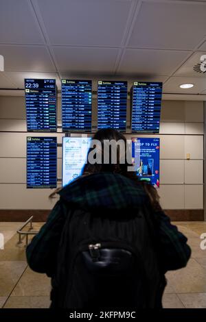 La giovane donna in piedi con il suo zaino guarda il programma alla stazione dell'aeroporto. Trasporto pubblico a tema. Foto Stock