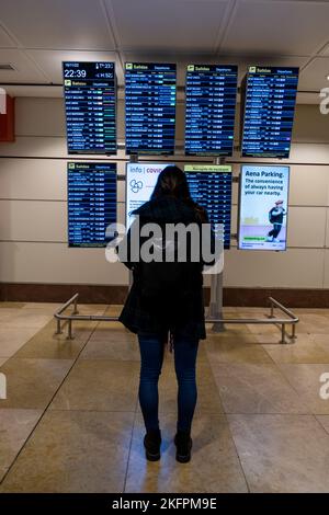 La giovane donna in piedi con il suo zaino guarda il programma alla stazione dell'aeroporto. Trasporto pubblico a tema. Foto Stock