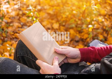 Un uomo tiene un libro con uno spazio vuoto nella natura autunnale. Spazio per la copia del libro. Il concetto di leggere libri in natura. Spazio libero per la pubblicità. Foto Stock