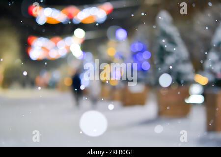 Sfondo sfocato astratto. Molti degli alberi di Natale decorati si ergono lungo la strada decorata con illuminazione luminosa, luci scintillanti e ghirlande in città durante le pesanti nevicate nella notte d'inverno Foto Stock