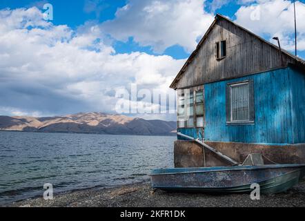 Vecchia casa di legno e una barca sulle rive del lago Sevan in Armenia. Foto Stock