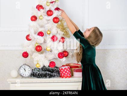 Bambino appendere palla ornamento di natale su albero artificiale. I capretti possono illuminare in su l'albero di natale generando i loro propri ornamenti. Ragazza celebrare il natale Foto Stock