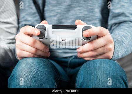 Bambino adolescente irriconoscibile seduto a casa, con il controller di gioco bianco joystick gamepad, giocare a videogiochi sulla console di gioco. Hobby, gratuito Foto Stock