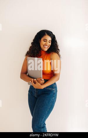 Imprenditore femminile di successo sorridente felicemente mentre in piedi contro uno sfondo della parete. Giovane donna d'affari allegra che tiene un notebook in un wor moderno Foto Stock