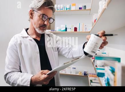 Farmacista maturo che legge un'etichetta del farmaco in una farmacia. Operatore sanitario senior che dispensa le prescrizioni in farmacia. Foto Stock