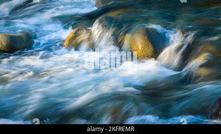 Ruscello di montagna precipita sulle rocce fluide del fiume con striature d'acqua contro le pietre calde colorate Foto Stock