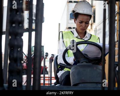 Ingegnere caposquadra personale dipendente bianco casco di elmetto sit carrello elevatore conducente donna donna donna pelle nera persona africana importazione esportazione log di spedizione Foto Stock