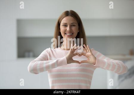 Giovane donna sorridente che mostra il segno del cuore con le dita Foto Stock