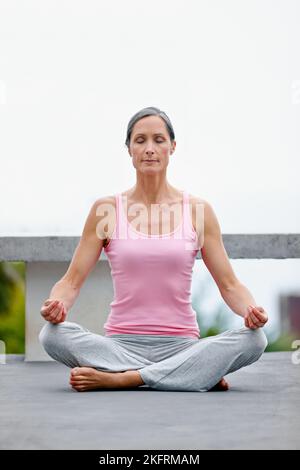 Fare il tempo di meditare. Una donna matura attraente che pratica yoga nella posizione del loto. Foto Stock