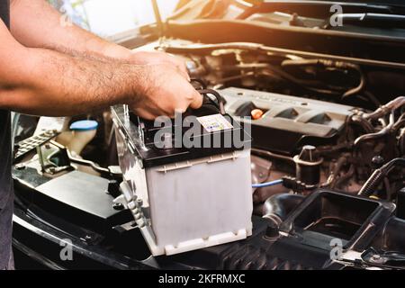 Un meccanico auto porta una batteria di ricambio per auto per la manutenzione elettrica Foto Stock