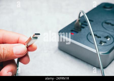 Mano umana che tiene un cavo di ricarica per telefono cellulare di tipo C collegato a una presa di ricarica usb Foto Stock