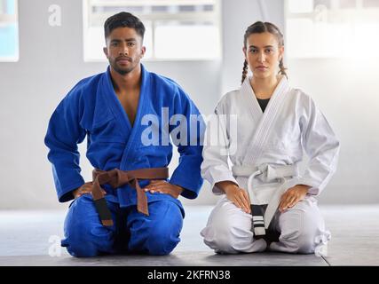 Karate, uomo e donna in ritratto insieme alla determinazione del fuoco per il fitness, il benessere o l'allenamento. Coppia, arti marziali e ginocchia seduta in palestra Foto Stock
