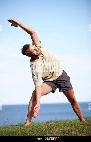 La sua routine quotidiana di esercizio in natura. Scatto completo di un bell'uomo maturo che fa yoga all'aperto. Foto Stock