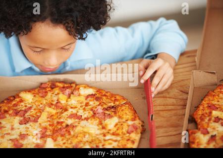 La pizza hawaiana è la migliore. Un ragazzo carino che guarda la pizza davanti a lui. Foto Stock