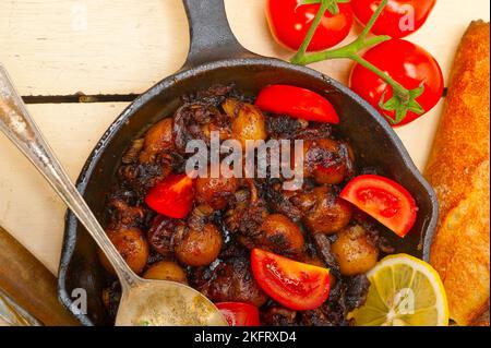 Baby seppie arrostite in padella di ferro con pomodori e cipolle su tavola in legno rustico Foto Stock