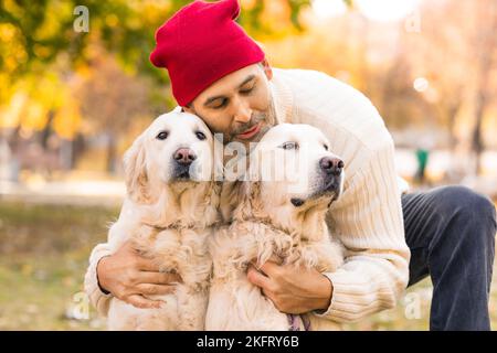 Primo piano di un uomo di mezza età che bacia i suoi due cani, Golden Retriever. Amicizia, amore e cura per gli animali domestici. Foto Stock