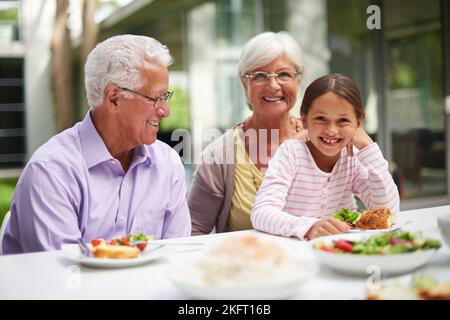 Pranzo con nonno e nonno. Una nipote seduta con i nonni mentre si gustava un pasto all'aperto. Foto Stock
