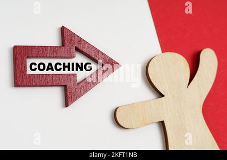 Economia e business concept. Su una superficie rosso-bianca, una figura umana e una freccia con l'iscrizione - COACHING Foto Stock