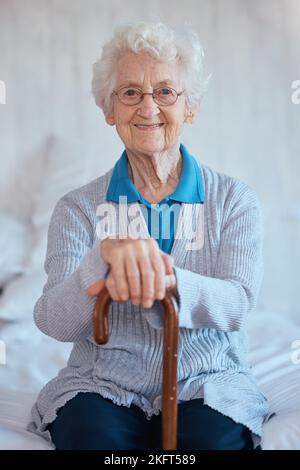 Donna anziana, seduto ritratto e sorriso a letto con felicità, bastone da camminare e rilassarsi in casa di cura. Signora anziana felice, camera da letto e canna per Foto Stock