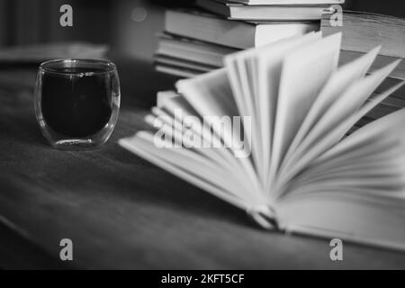 Pila di vecchi libri e tazza da caffè, in bianco e nero. Background letterario. Apri il libro e la pila di libri sul tavolo. Tempo caffè in biblioteca. Foto Stock