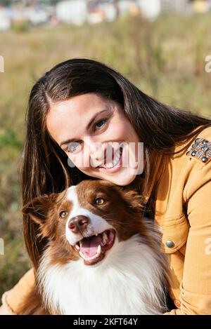 Giovane donna sorridente in abiti casual con adorabile bordo Collie guardando la macchina fotografica nel parco nella giornata di sole Foto Stock