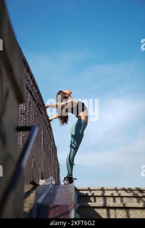 Vista laterale ad angolo basso della giovane atleta in abbigliamento sportivo che si allunga sulle scale durante gli allenamenti all'aperto nelle giornate di sole Foto Stock
