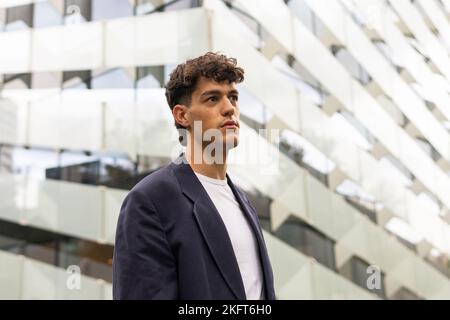 Giovane imprenditore maschile in abiti casual elegante guardando lontano contro il grattacielo moderno sulla strada del centro città Foto Stock