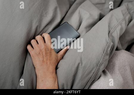 Angolo alto di anonima signora anziana sdraiata su un comodo letto e navigare in internet tramite cellulare Foto Stock