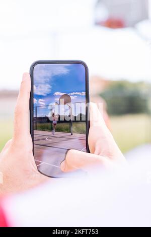 Primo piano di un anonimo uomo che scatta foto con il telefono di sport giocare a basket in campo sportivo Foto Stock