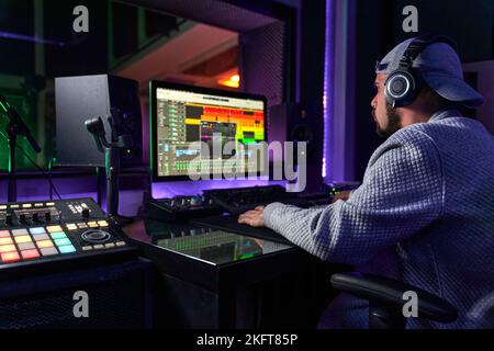 Vista posteriore di anonimo ingegnere audio maschile utilizzando il computer durante la registrazione di canzone del cantante in piedi in studio Foto Stock