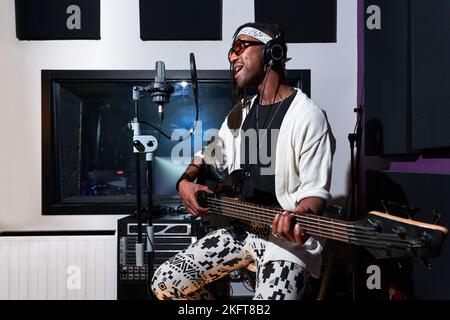 Musicista afro-americano maschio con Dreadlocks che suona chitarra elettrica e canta vicino al microfono durante le prove in studio professionale Foto Stock