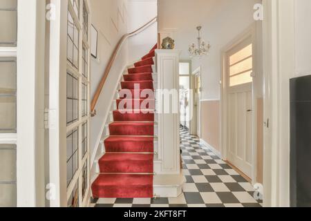 Scalinata con moquette rossa e pavimento in mosaico bianco e nero a casa Foto Stock