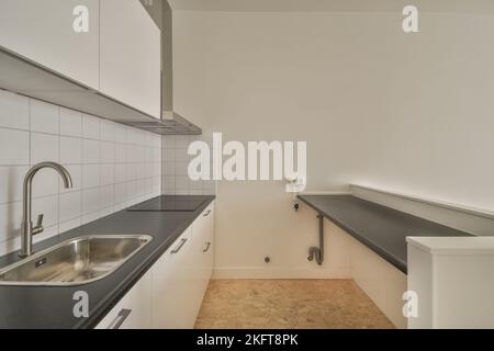 Banconi bianchi con lavello situato contro la parete con mobili da incasso in cucina leggera a casa Foto Stock