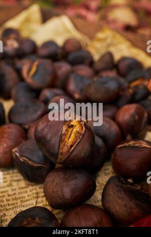 Dall'alto ravvicinato su palo di castagne fresche cotte su vassoio di legno vicino a foglie asciutte sul terreno nella foresta autunnale Foto Stock