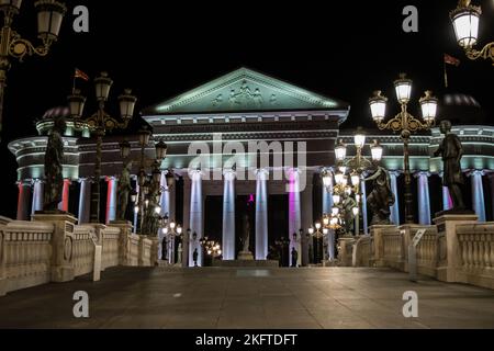 Statue che decorano il Ponte delle civiltà, di fronte al Museo Archeologico di Skopje, Macedonia settentrionale. Di notte con lampioni che illuminano il ponte. Foto Stock