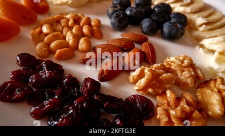 Frutta fresca e secca con teglia a nocciola, mirtilli rossi secchi, mandorle, noci e arachidi, mirtilli sul piatto bianco. Foto Stock